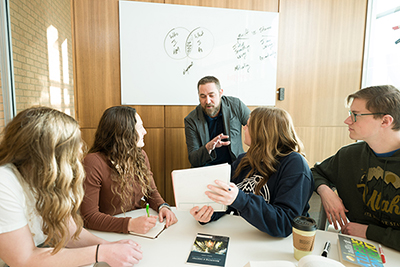 A professor teaching a small group of students sitting at a table.