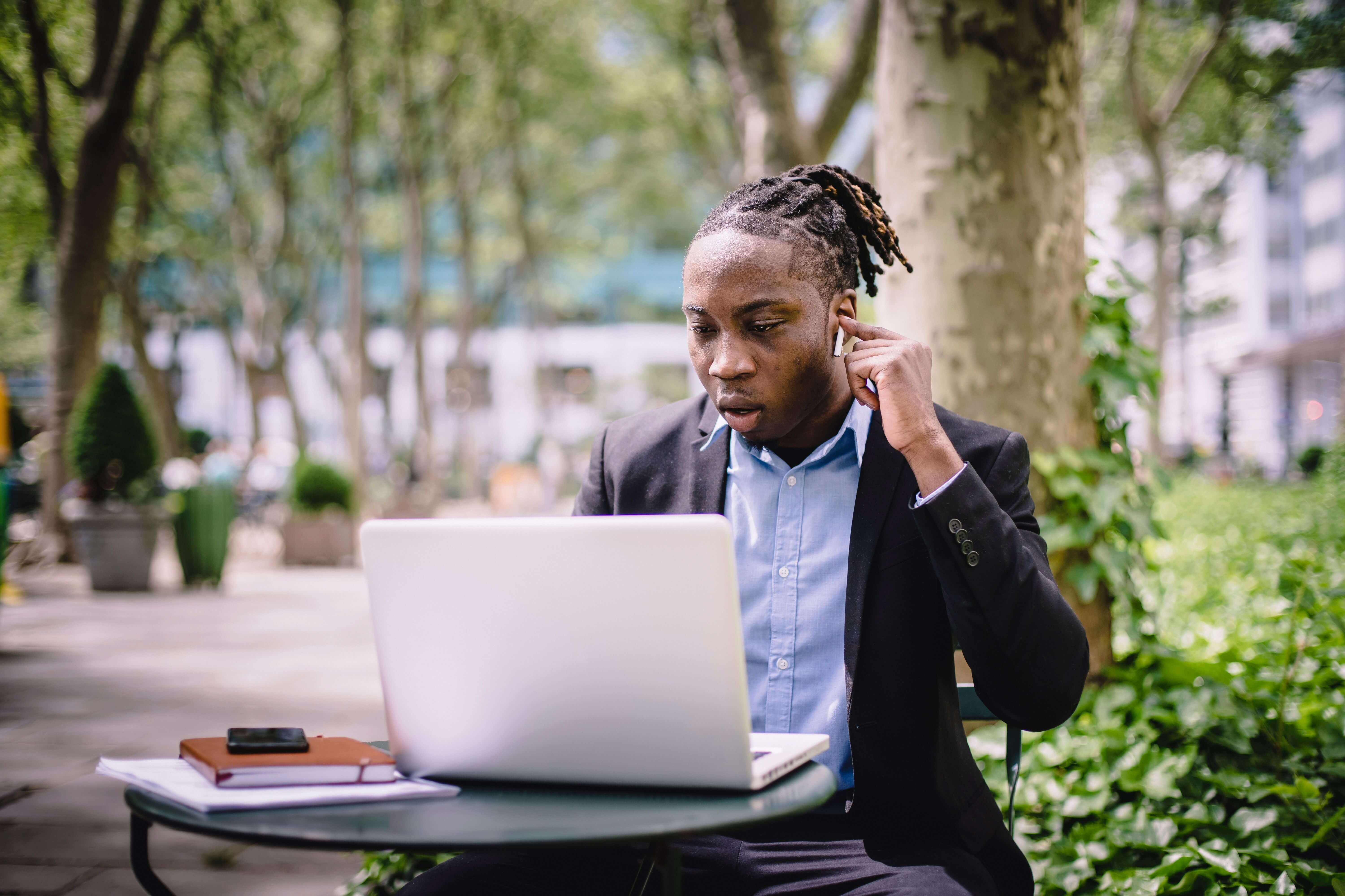 A man sitting at a table looking at his laptop with headphones in.