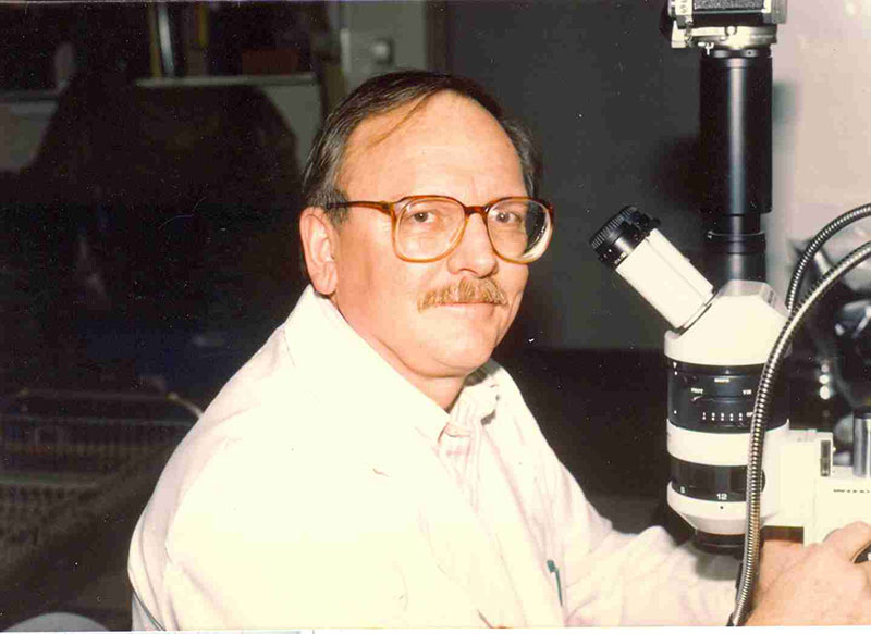 Side profile picture of Donald Roberts with a microscope on his desk