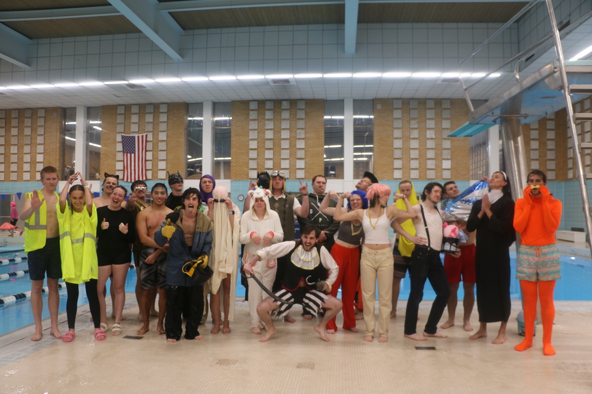 group of people standing outside an indoor pool, wearing halloween costumes