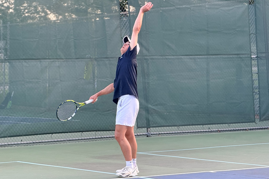 Boy serving a tennis ball on a tennis court outside