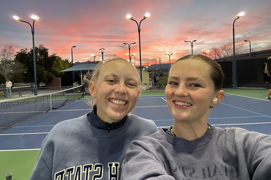 Two girls smiling at sunset on tennis court