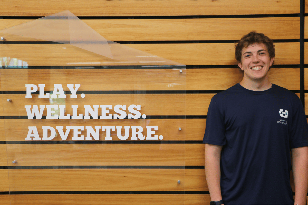 male personal trainer standing by a sign that says "play, wellness, adventure"