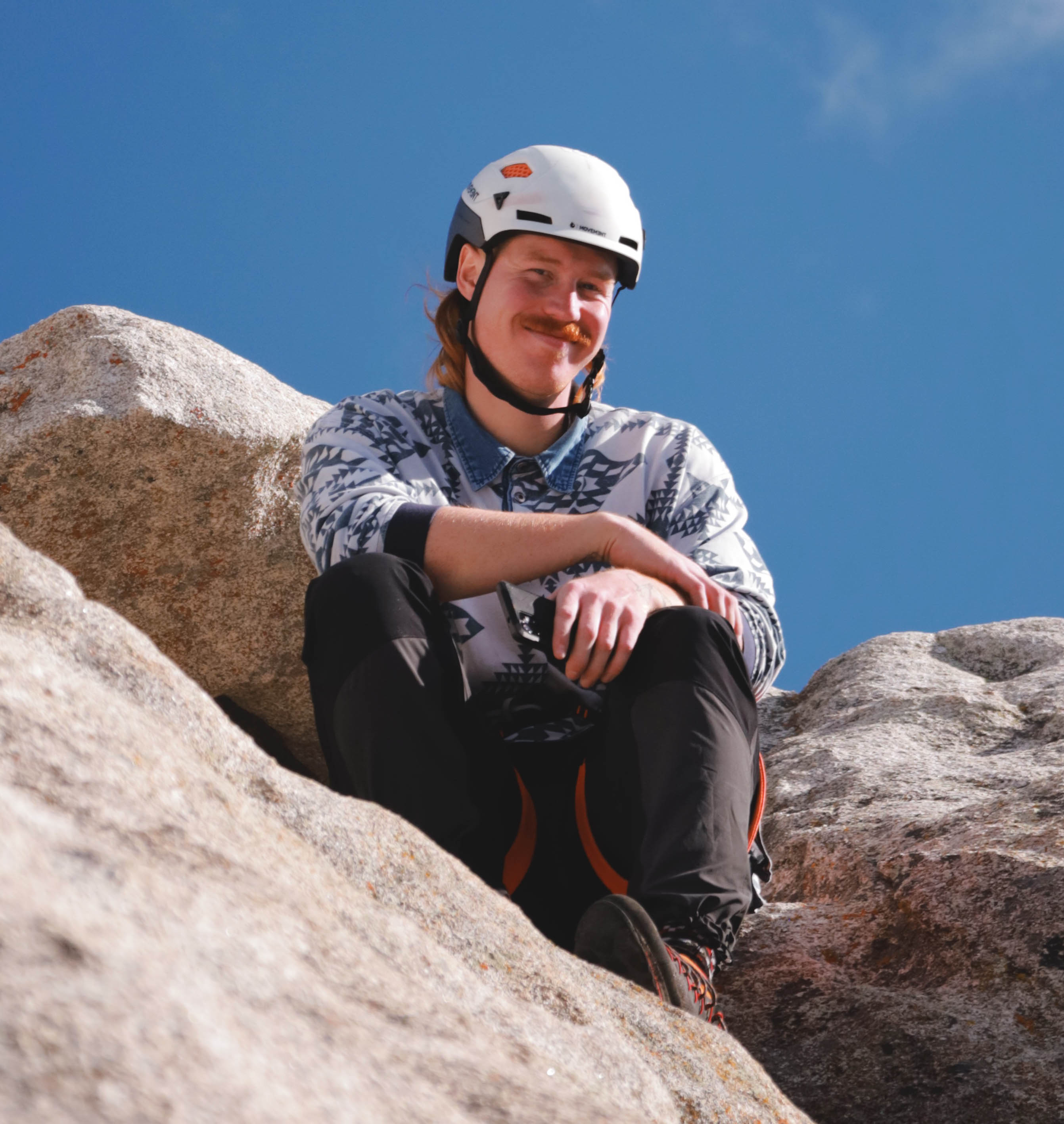 Theo sitting on a rock with a rock climbing helmet on smiling