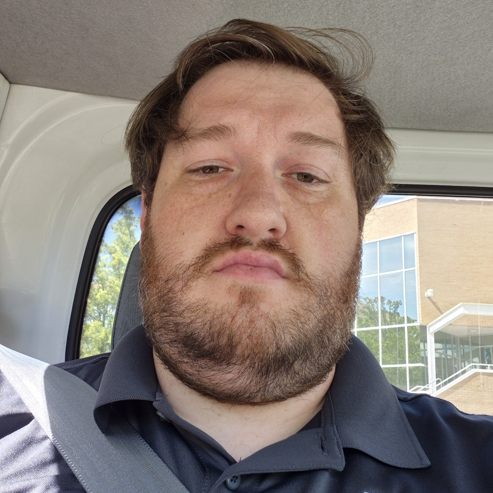 Bearded man taking a selfie in a vehicle, wearing a seatbelt