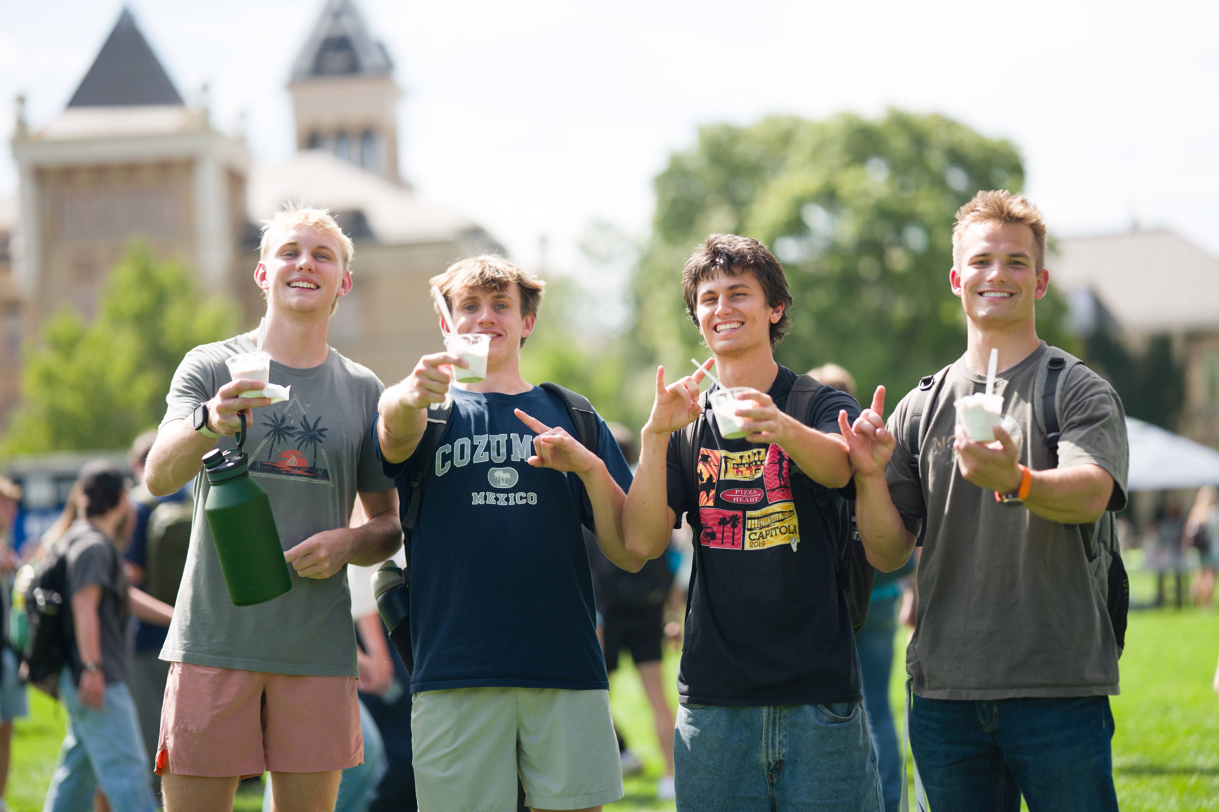 a group of four boys enjoying cups of ice cream on the quad. They are all smiling at the camera