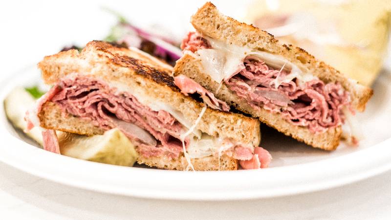 pastrami sandwich laying on a plate with a pickle spear