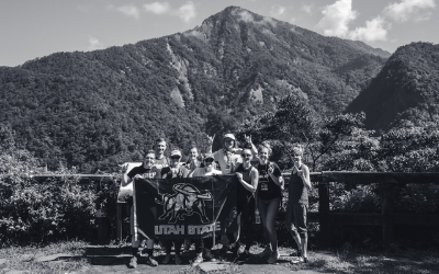 With a Taiwanese mountain in the background, Alumnus Garrett Brogan and other alumni hold a USU flag