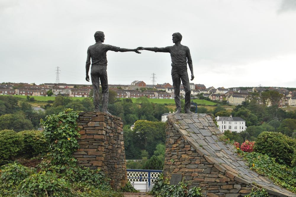 sculpture of two men across from each other touching hands over the divide