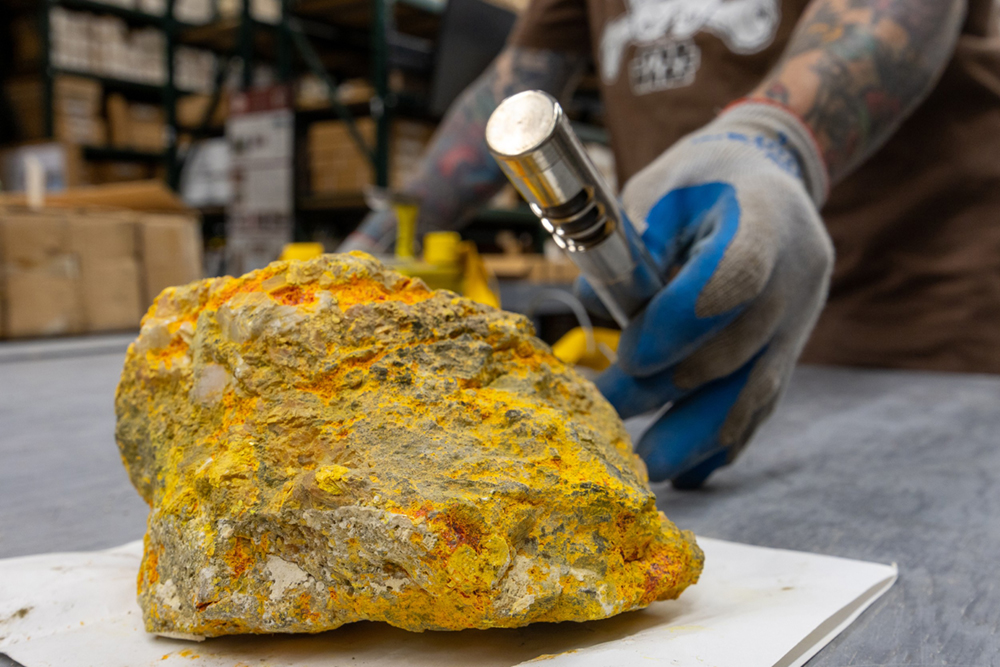 Raw Uranium Ore on a table being inspected using a metal device