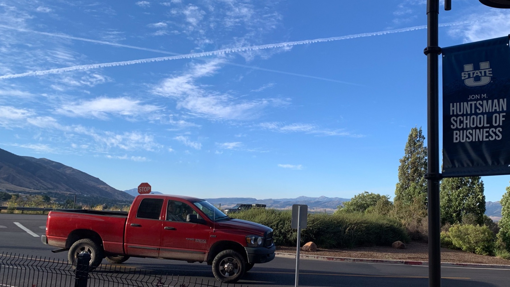 Two contrails shooting across the sky above a red truck and a Jon M. Hunstman School of Business banner