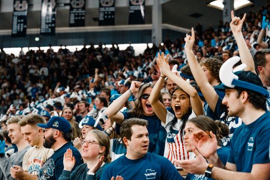 A cheering crowd in a stadium, with several people in the foreground raising their hands and looking excited. This image links to the Memorable HURD Moments page.
