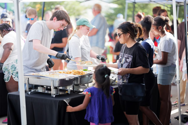 lines of people getting food from outdoor vendor tables on Juneteenth 
