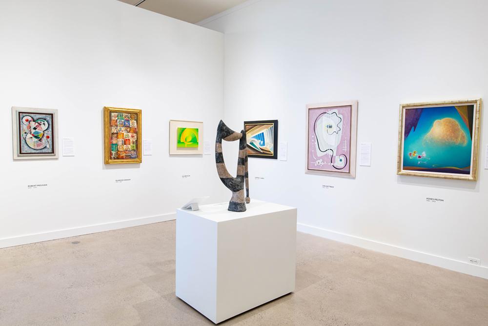 An exhibition corner with a sculpture set on a presenting table and art pieces hung on the wall behind