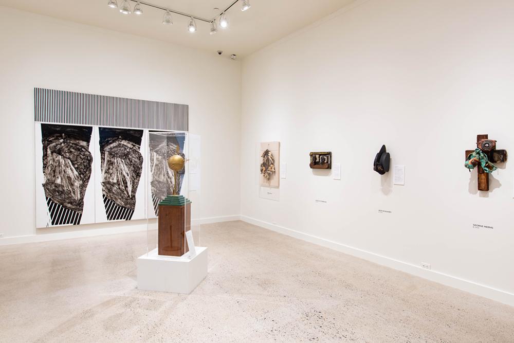 A corner with a main sculpture in the middle and five art pieces hung on the two walls behind