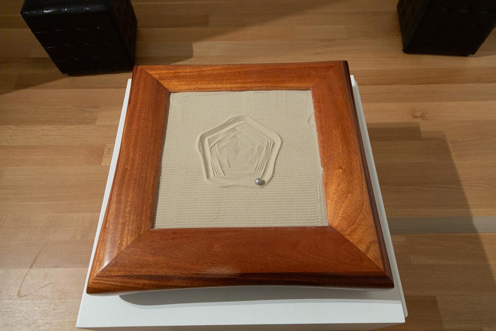 A pentagon pattern drawn in sand with a metal ball