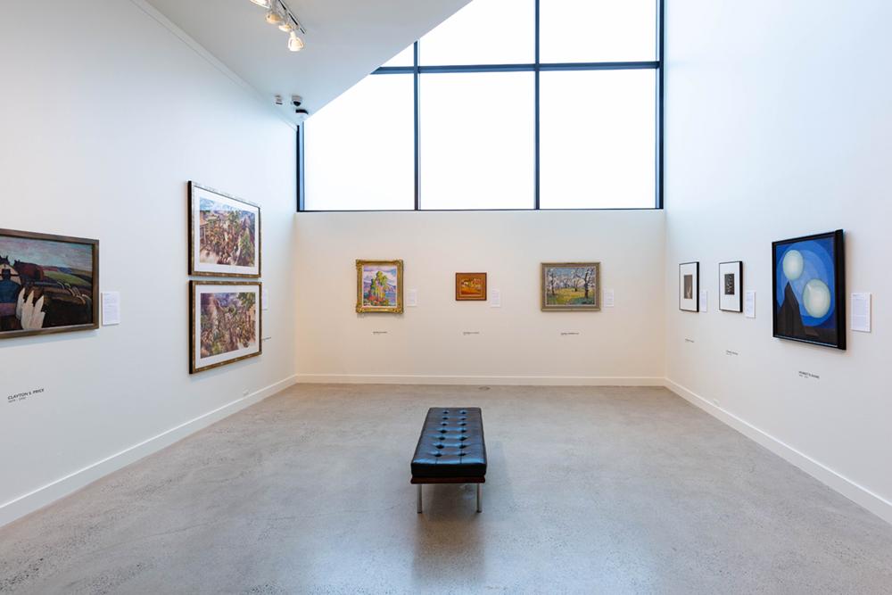 Three walls of the exhibition each with three art pieces hung on the wall and a bench in the middle of the room