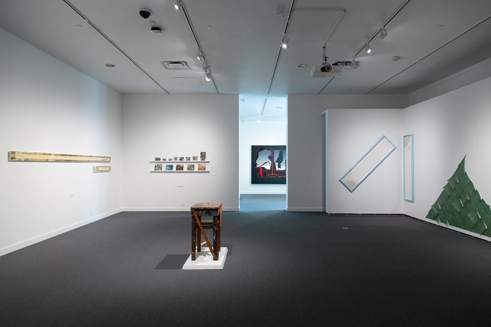 A sculpture of a stool in the middle of the room with various art pieces on the walls