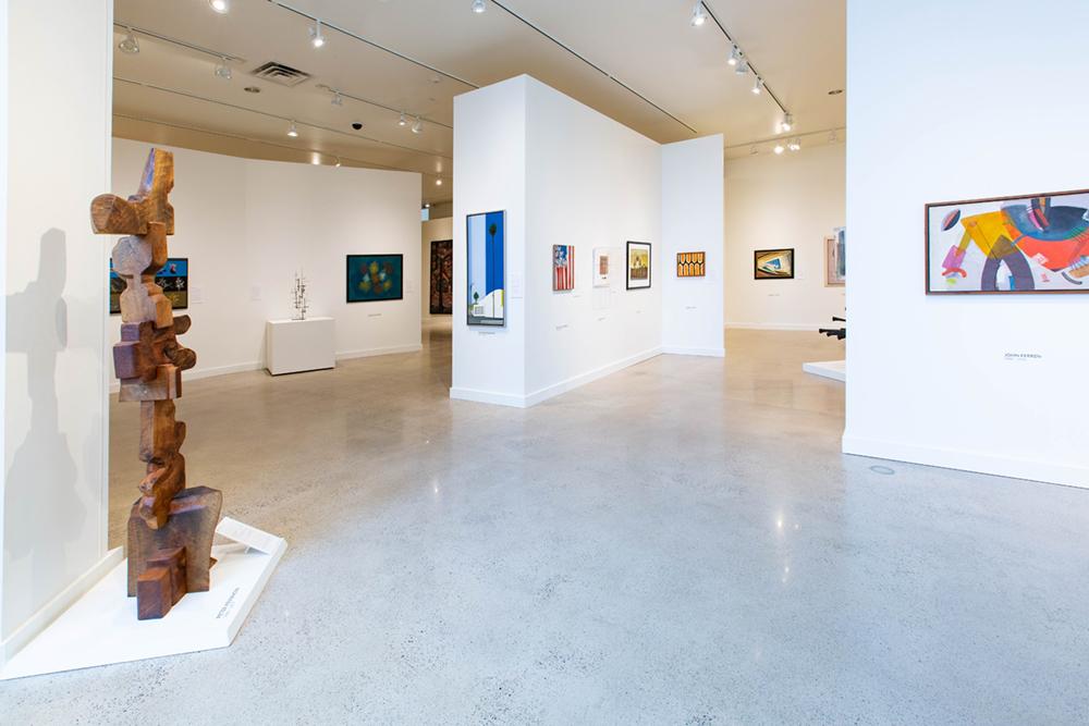 A view of various exhibit spaces with a sculpture on the left and an assortment of art pieces on the walls