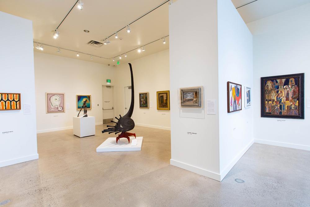 A view of various exhibit wall spaces with a sculpture in the middle and assorted art pieces on the walls