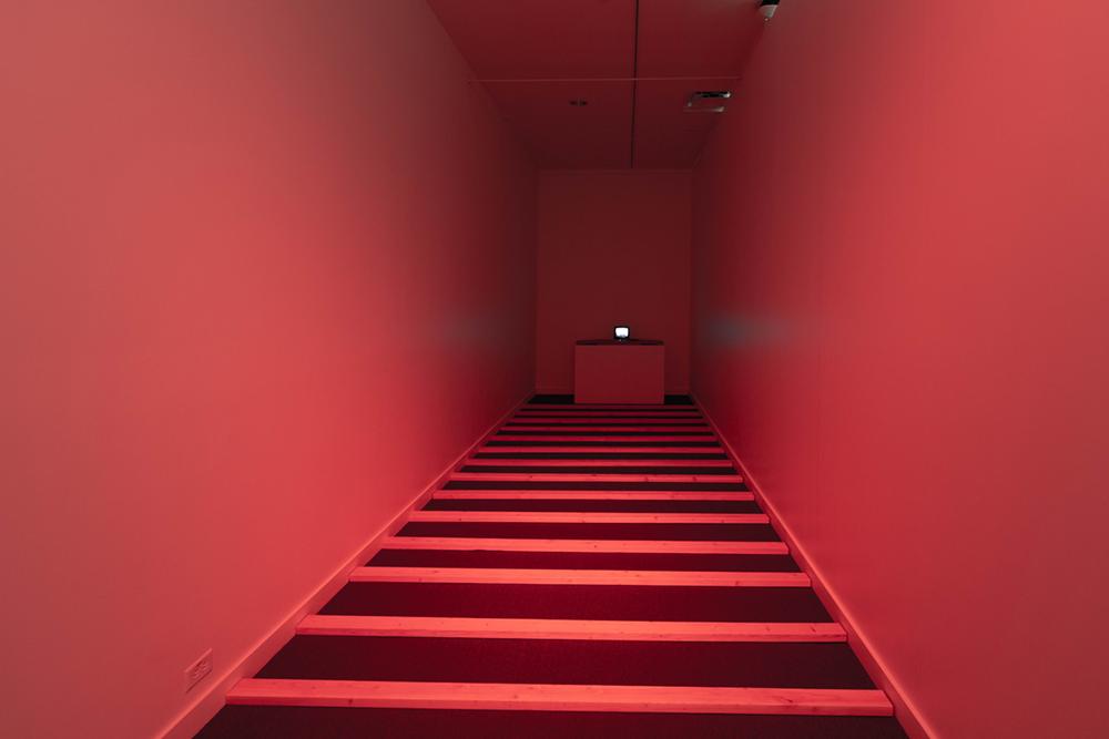 A completely red lit dead end hallway with boards laid striping the ground 