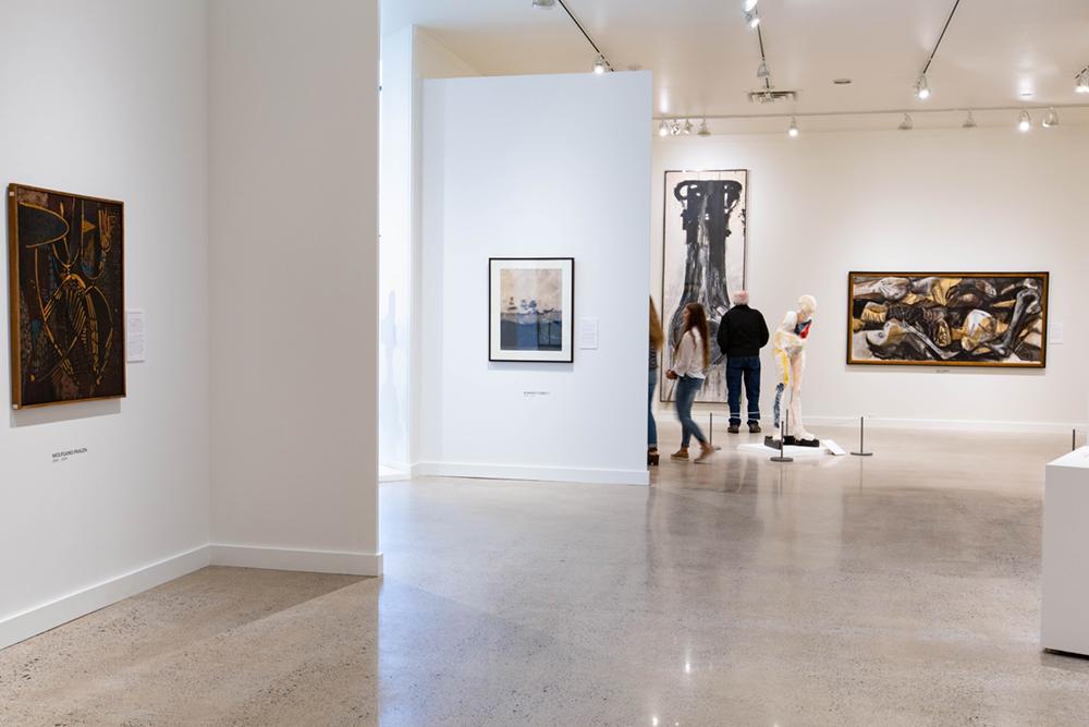 Walls of the exhibition with art on them and people observing the pieces