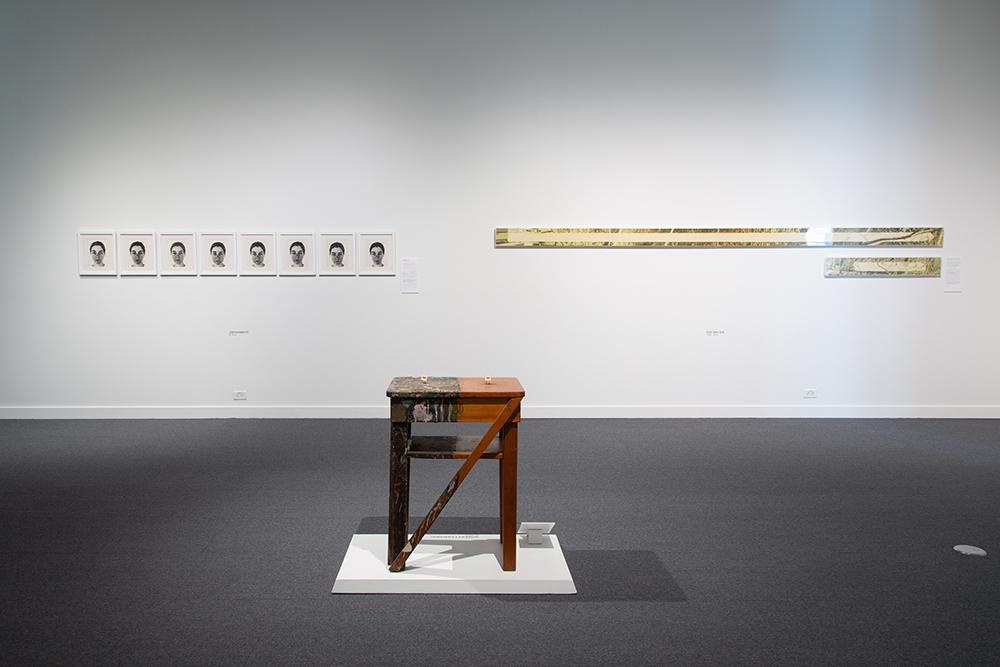 A sculpture of a stool in the middle with two art displays hanging on the wall behind