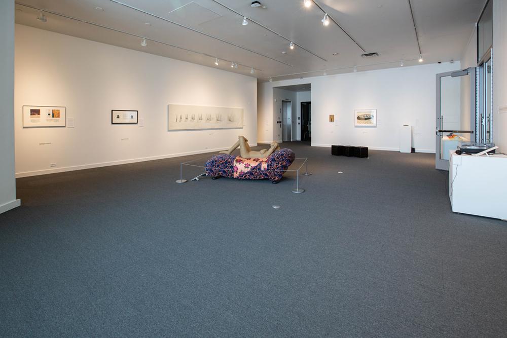 An open space with art on the wall and a human form sculpture laying on a settee