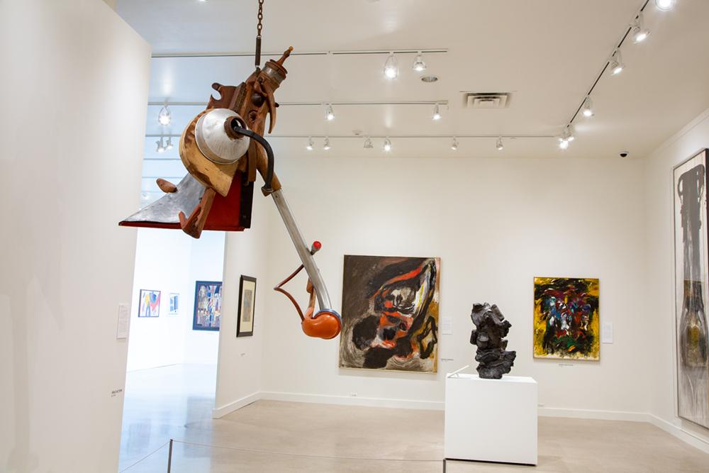 An abstract sculpture hangs from the ceiling with art pieces hung on the wall behind