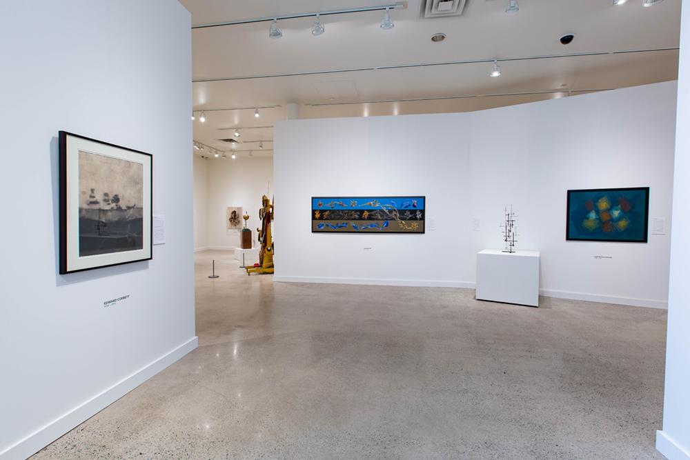 An open area of the exhibition with three art pieces on the wall and a small sculpture set on a presentation table