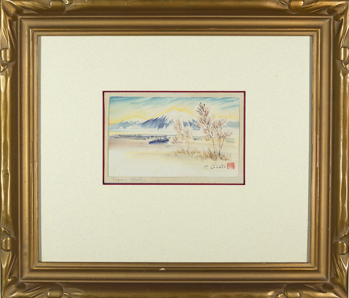 A golden framed piece depicting a blue and white mountain range in the distance and shrubbery in the foreground