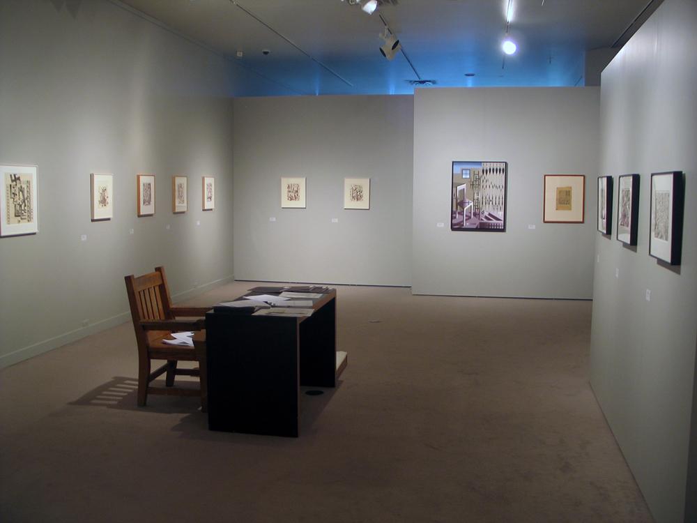 A desk with a wooden chair in the middle of an exhibition room
