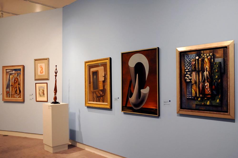 Large framed art pieces hang on the wall with a wooden sculpture on white display table