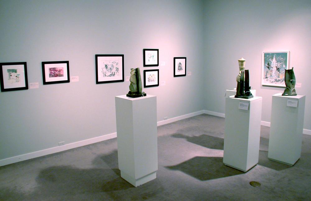A view of an exhibition corner with art on the wall and on white display tables