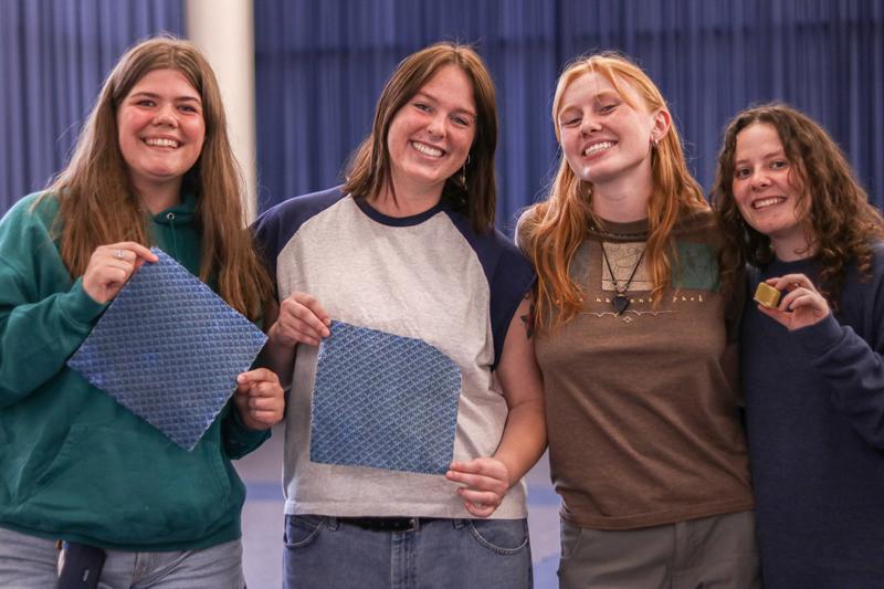 Four students standing side-by-side and smiling while two hold up their new beeswax wraps and one holds up a piece of beeswax.