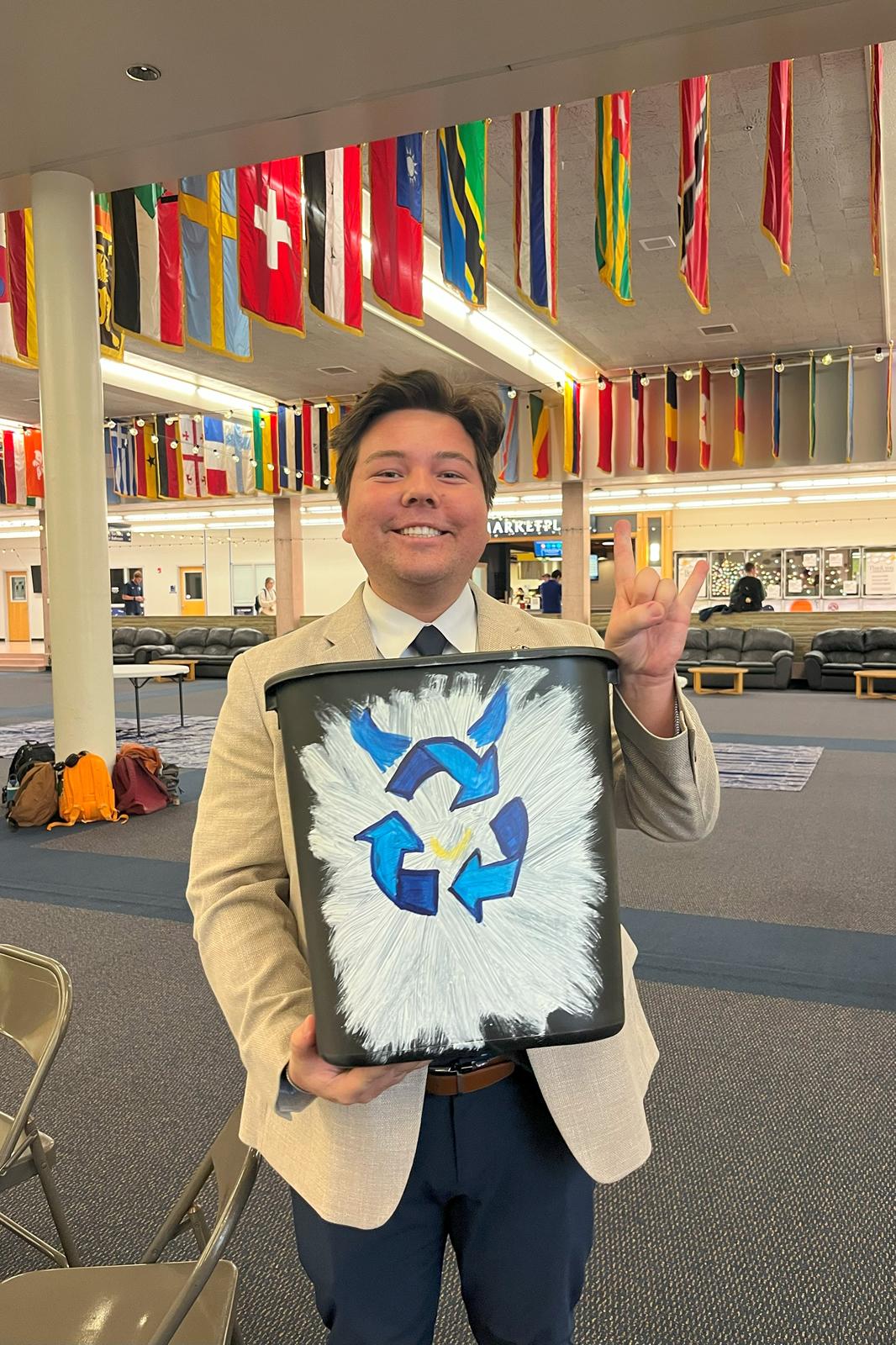USUSA President Brandon Sorenson holding up their recycling bin with the recycling symbol with Big Blue's horns.