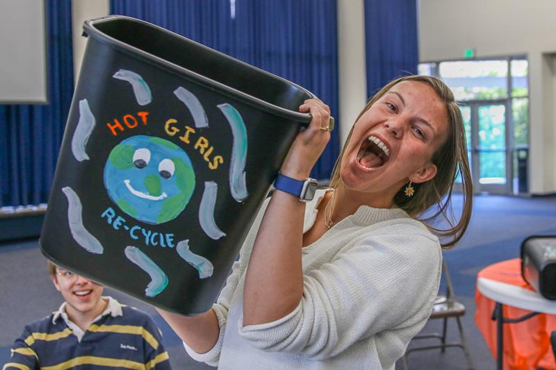 Third picture of student holding up their completed recycling bin painted with a smiling Earth surrounded by the words "Hot girls re-cycle".