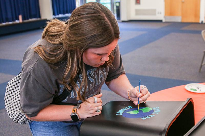 Student painting their recycling bin with an Earth design.