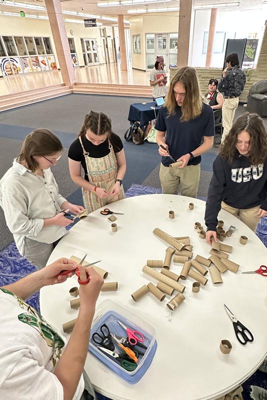 Students cutting and folding empty paper towel tubes and toilet paper tubes.