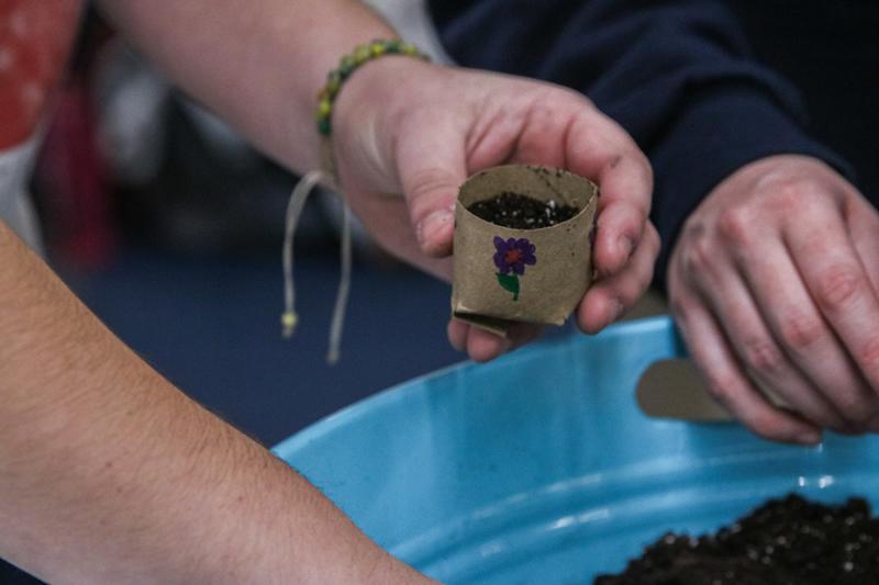 Closeup of hands packing soil into a toilet paper tube pot with a flower drawn on the pot.
