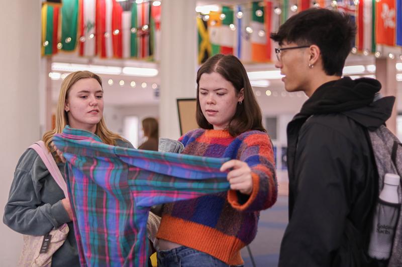 Three students talking and looking at a shirt.
