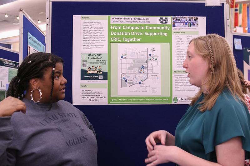 Two students talking about a poster discussing community-engaged work with the Cache Refugee Immigrant Connection.