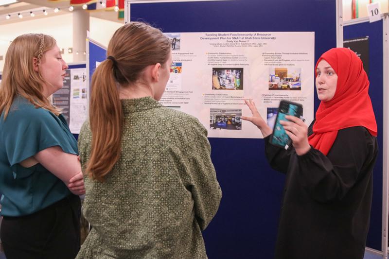 A student talking to two people about their poster discussing their community-engaged work with USU's Student Nutrition Access Pantry.