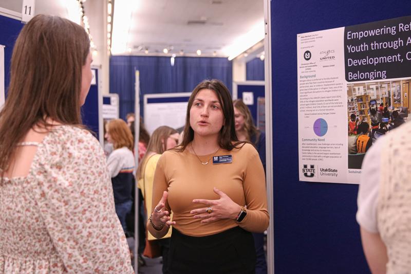 A student talking to someone about their poster discussing their community-engaged work with youth.
