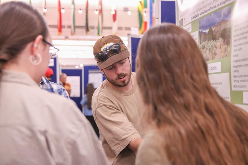 A student talking to two people about their poster discussing their community-engaged work with natural resource planning and management.