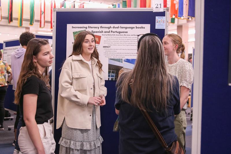 Two students talking to two people about their poster discussing their community-engaged work with increasing literacy through dual-language books.