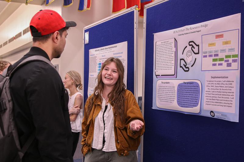 A student talking to someone about their poster discussing their community-engaged work with USU's REACH Peer Program.