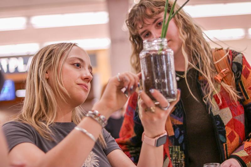 Two students looking at a plant freshly planted in a reused glass jar and soil.
