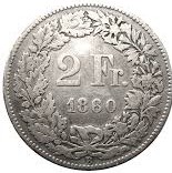 A silver coin displaying “2 Fr.” and the year 1860 in the center. The text is surrounded by a detailed wreath design with leaves and small flowers around the edge. The coin has a ridged border.