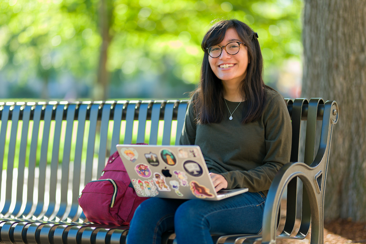Female student smiling at the camera while studying on a park bench